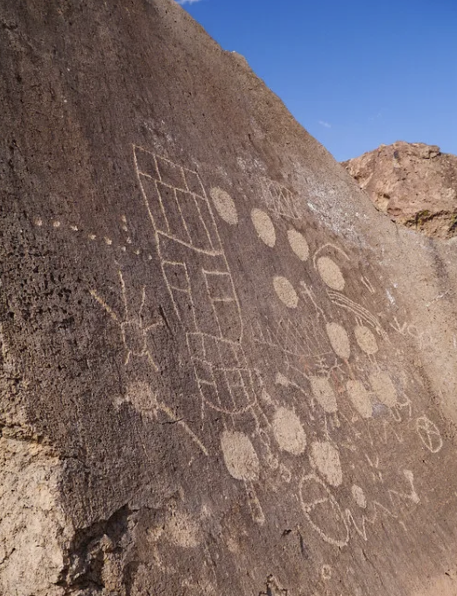 A reddish coloured rockface with 13 pale moons in a half circle, with an image of the sun to the left and the appearance of rectangular fields or planting zones.